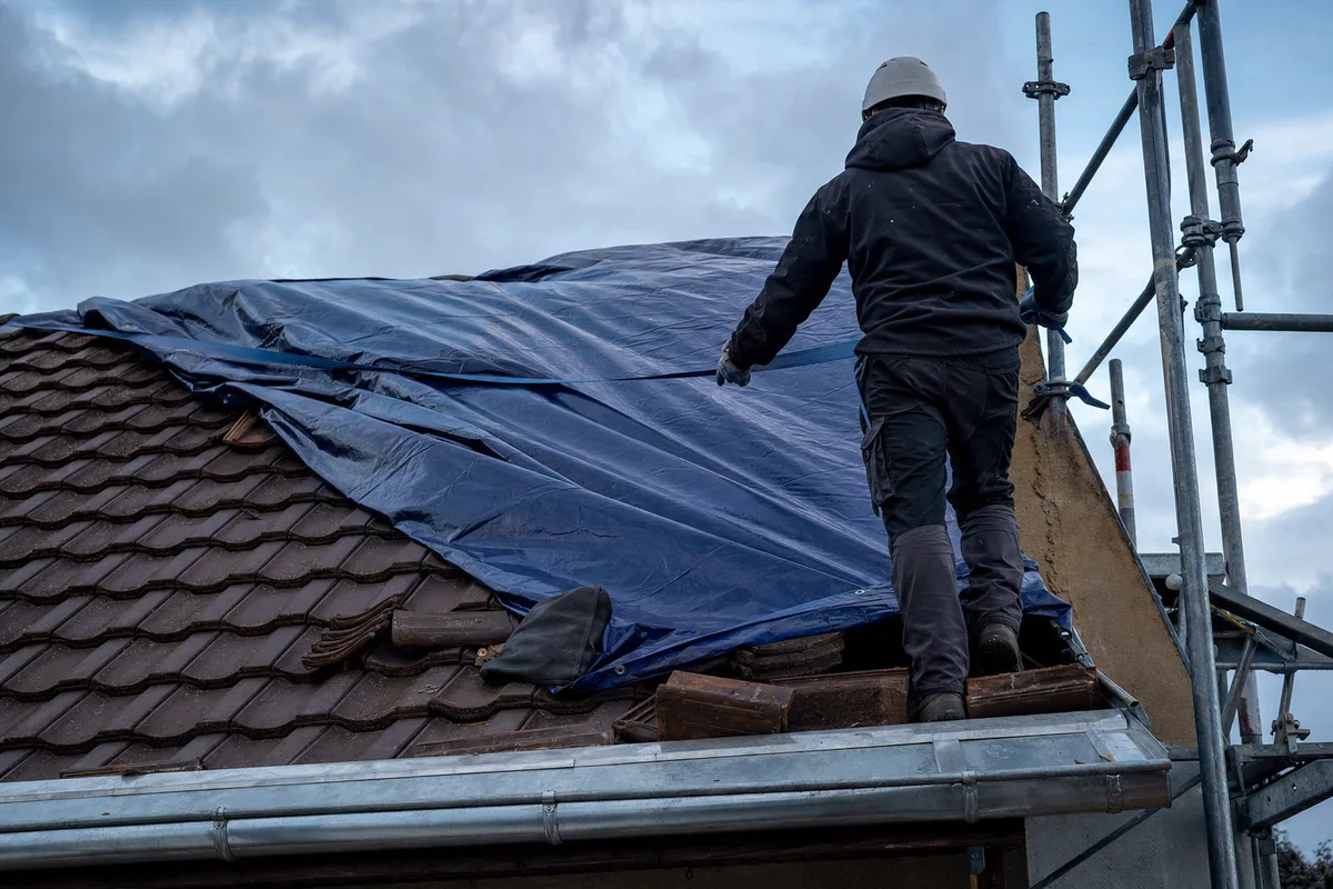 Bâchage de sécurisation posé sur un versant de toiture après une tempête, gouttière et échafaudage en premier plan