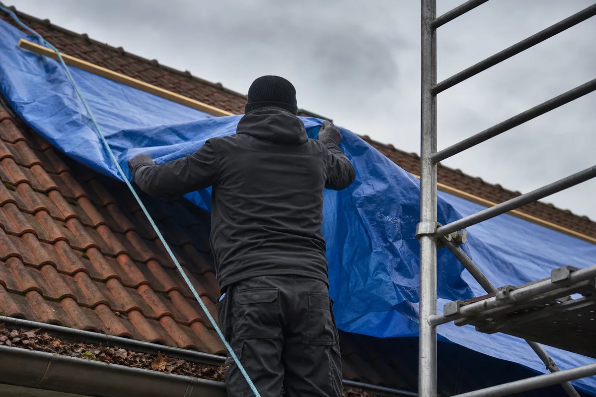 Couvreur de dos posant une bâche de protection sur un versant de toiture francilien